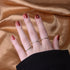 Hand with burgundy nails modeling three thin gold rings with different gemstones against silk fabric