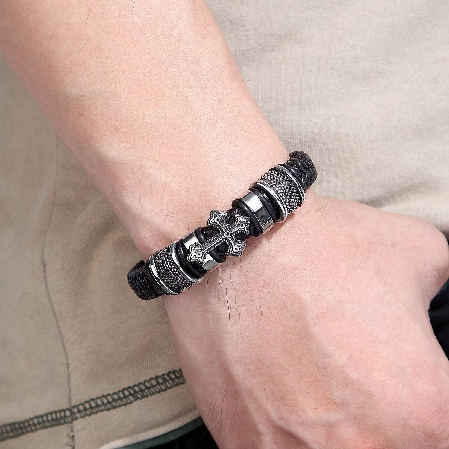 Black and silver cross bracelet worn on a wrist, featuring textured metallic accents.