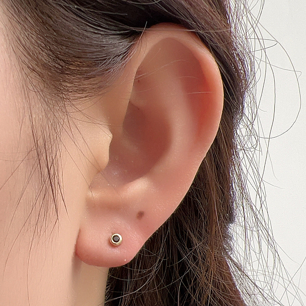 Delicate gold stud earring with black stone shown worn in earlobe, profile view