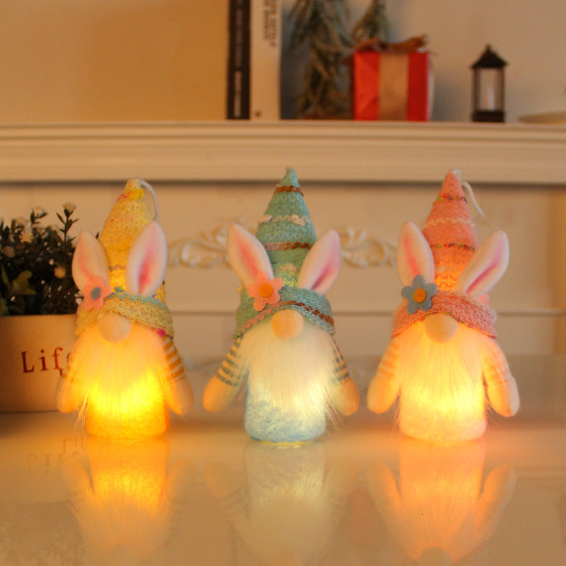 A trio of illuminated Easter bunny gnome figurines in blue, yellow, and pink, glowing softly on a white tabletop.