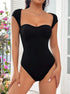 Full-body view: Sleek black bodysuit with cap sleeves and a contoured fit, styled with a minimalistic jewelry look.
