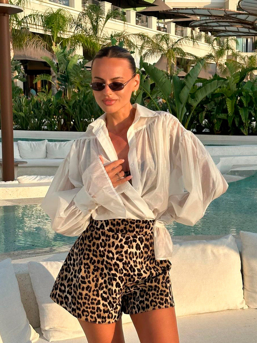 Woman with sunglasses near a pool, styling a sheer white blouse and leopard print shorts.