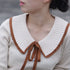 A woman wearing gold interlocking circles necklace with her cream sweater featuring brown-trimmed collar, showing how pendant sits at collarbone
