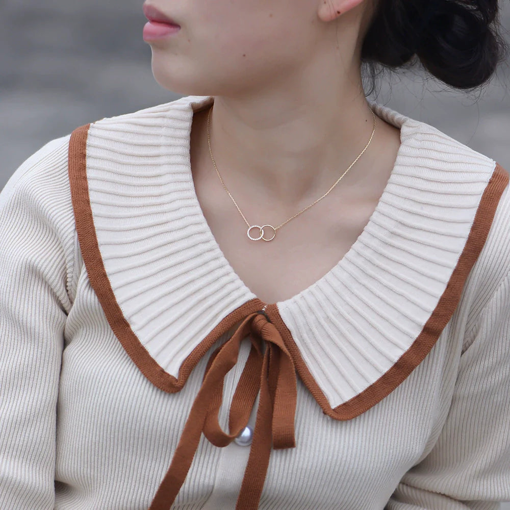 A woman wearing gold interlocking circles necklace with her cream sweater featuring brown-trimmed collar, showing how pendant sits at collarbone