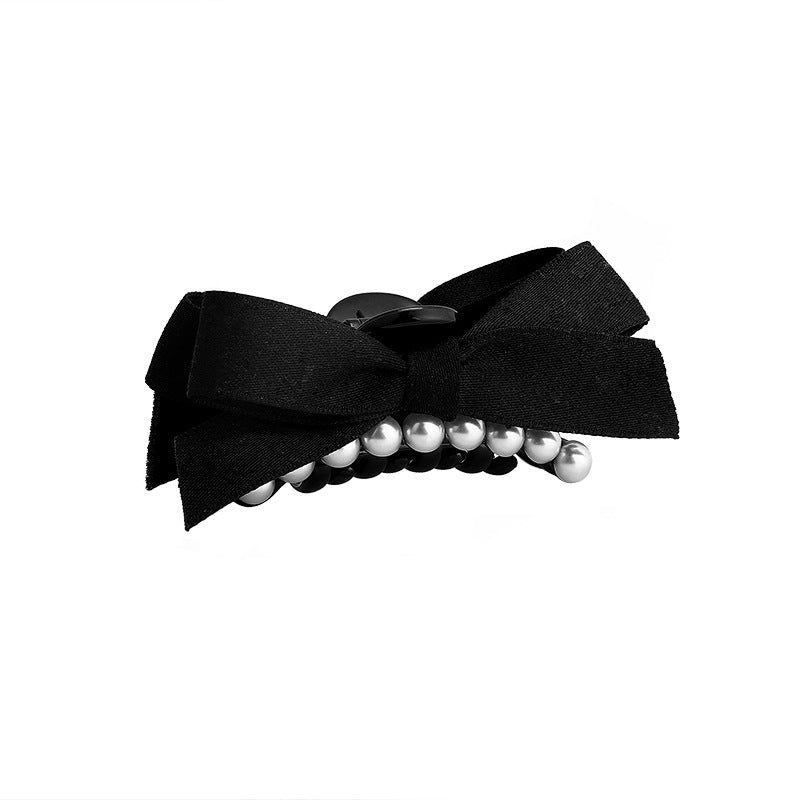 Close-up of a black hair clip with a black satin bow and pearl accent, showcasing the detailed design against a plain background