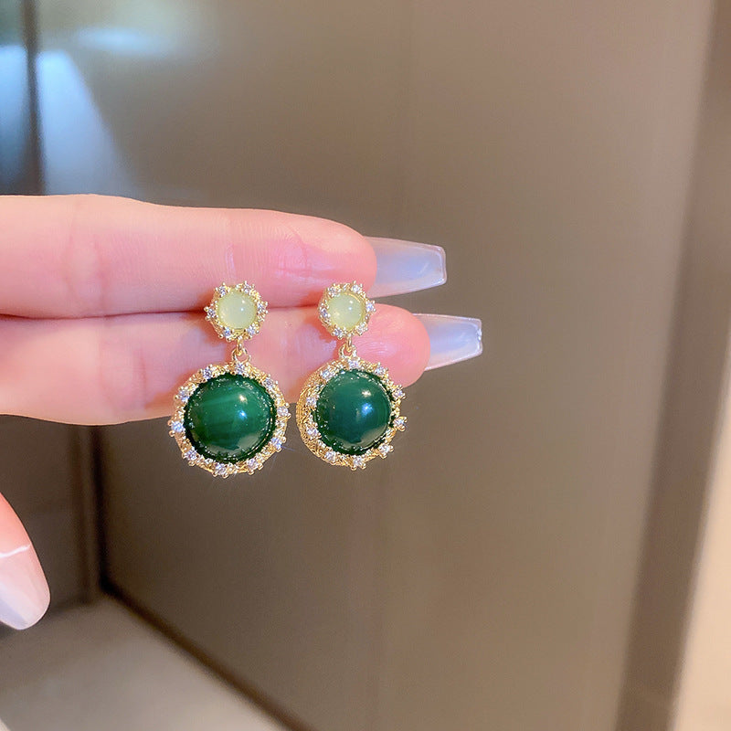 Minimalist gold hoop earrings with emerald green oval pendants displayed on white ceramic plate showing elegant everyday jewelry