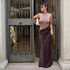 Fitted blush pink sleeveless top with high neck and draped dark brown floor-length skirt, worn by a woman standing by an ornate metal gate, carrying a white handbag and wearing sunglasses