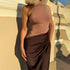 Fitted brown dress with high neck and asymmetrical draped skirt, photographed in sunlight with architectural shadows in the background