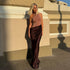 Nude and brown floor-length dress with fitted top and flowing draped skirt, photographed against a textured architectural background with soft lighting