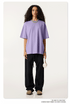 Female model in lavender oversized t-shirt paired with black pants, holding white headphones, wearing silver chain necklace and beige shoes