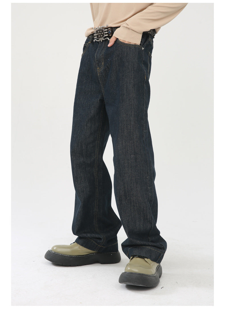 A model is posing with hand in pocket wearing dark denim straight-leg jeans with beige sweater, statement belt, and olive platform shoes