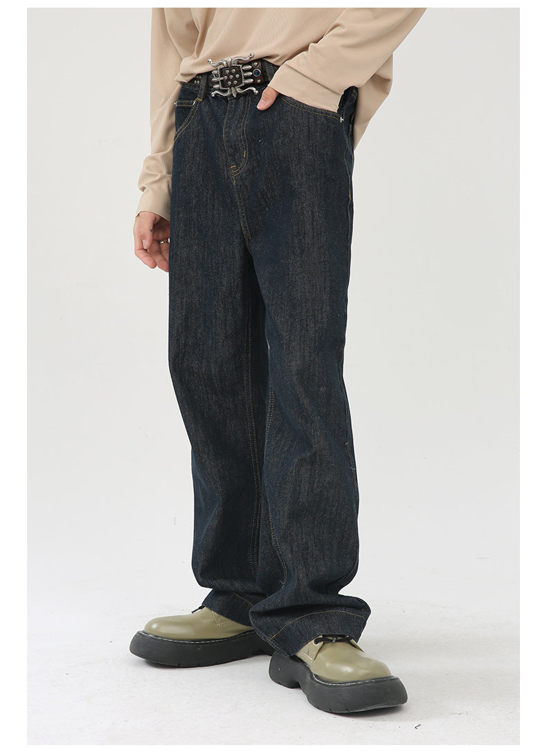 A model is standing wearing raw indigo wide-leg jeans paired with beige long-sleeve top and metal buckle belt against white background