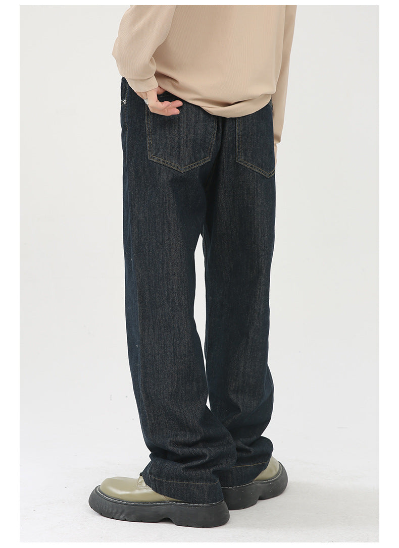 A model is showing the back view of dark indigo jeans with visible back pockets, beige sweater and olive platform shoes against white backdrop