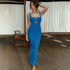 A woman wearing blue ruched bodycon dress with front cutout detail poses with hand in hair against white curtain background