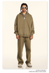 Model wearing olive tan oversized zip-up hoodie and matching relaxed sweatpants with white sunglasses, silver chains and beige shoes against cream backdrop