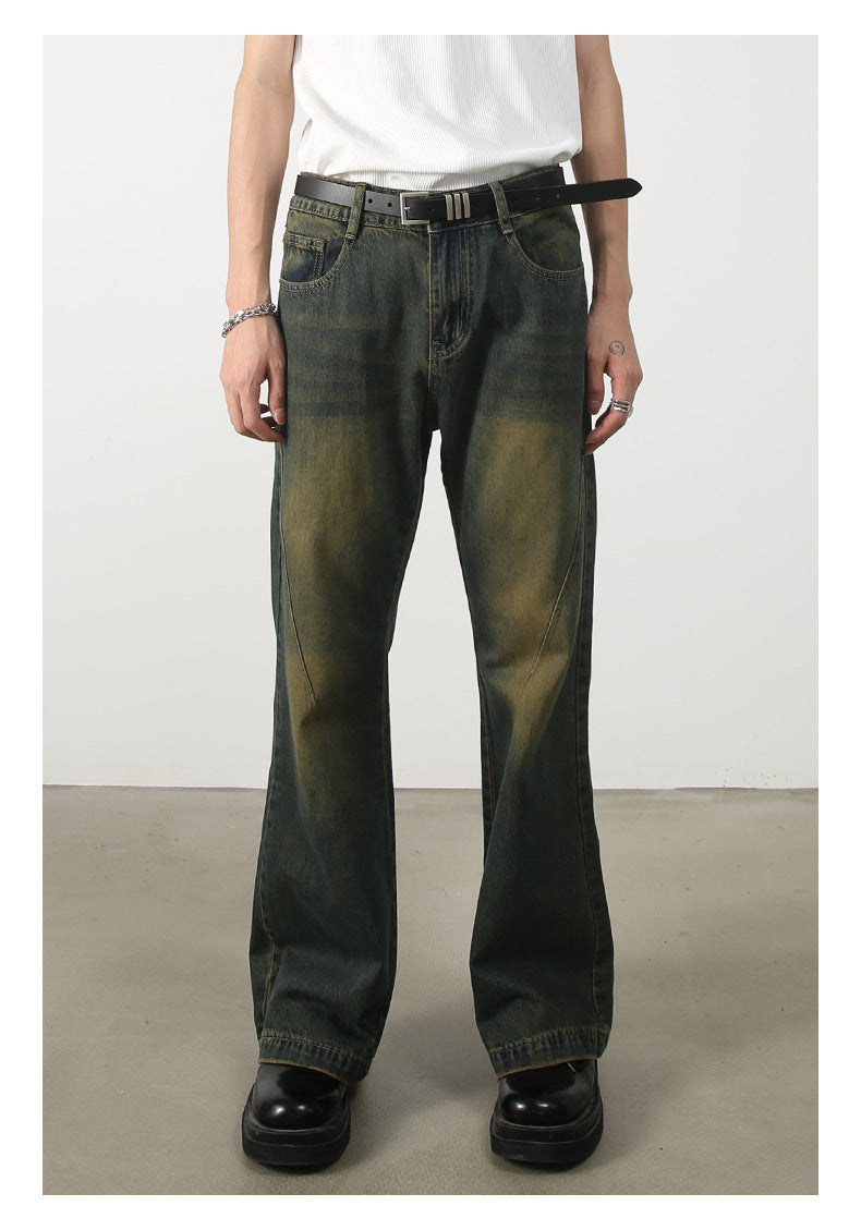 A person wearing olive-green wide-leg jeans with distinctive faded panels, white ribbed tank top, black leather belt with silver hardware, styled with chunky black platform shoes