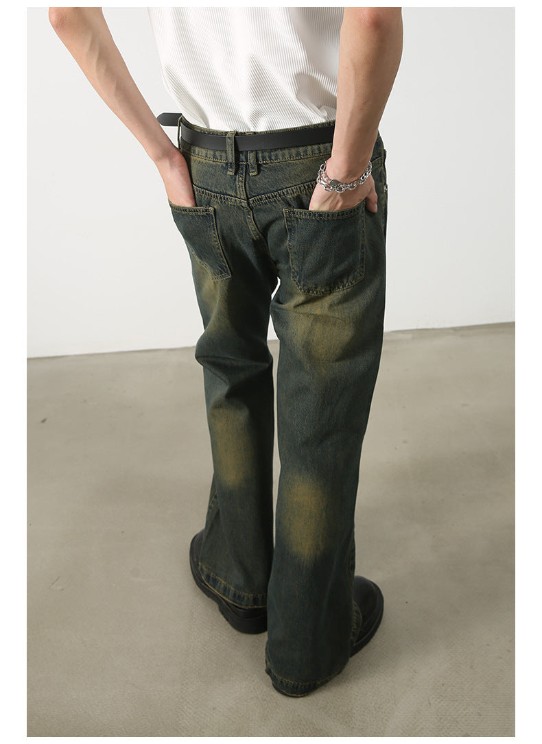 Rear view of person wearing olive-green wide-leg jeans with faded wash effect, white tank top, black belt, and silver chain bracelet with hands in back pockets