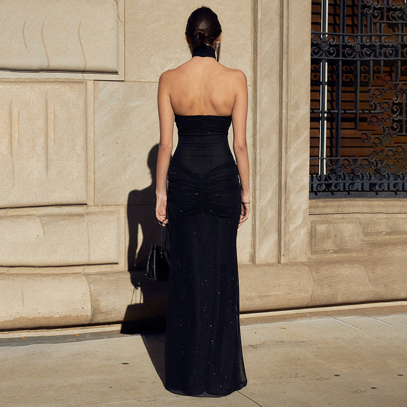 Back view of a woman wearing a strapless black evening gown with ruched details, standing in front of a textured stone wall