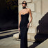 Woman in a black strapless evening gown with a choker, accessorized with sunglasses and a handbag, posing in sunlight