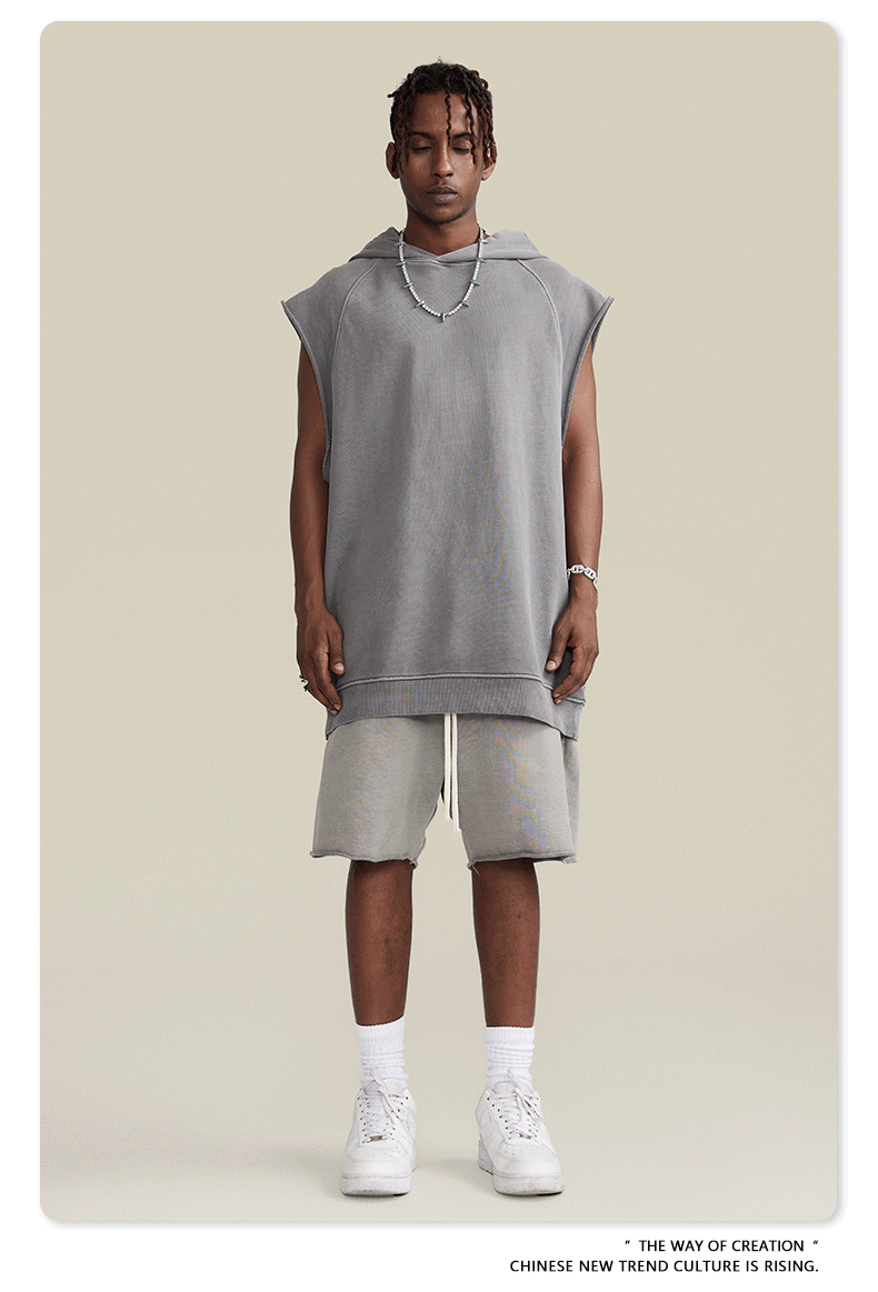 A model wearing light gray sleeveless hoodie with matching shorts, beaded necklace and white sneakers against neutral background