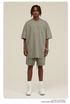 Man wearing sage green oversized T-shirt and shorts set with white sneakers and silver accessories