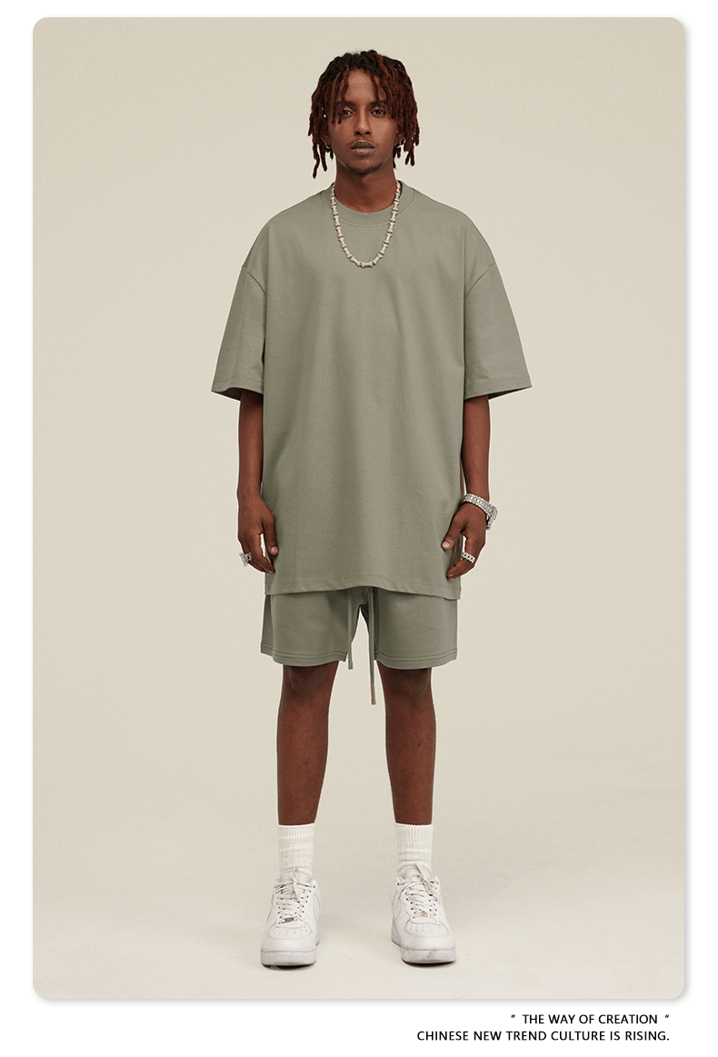 Man wearing sage green oversized T-shirt and shorts set with white sneakers and silver accessories