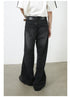 A back view of model in oversized white top and wide-leg black denim jeans. Shows detail of traditional back pockets and leather belt.