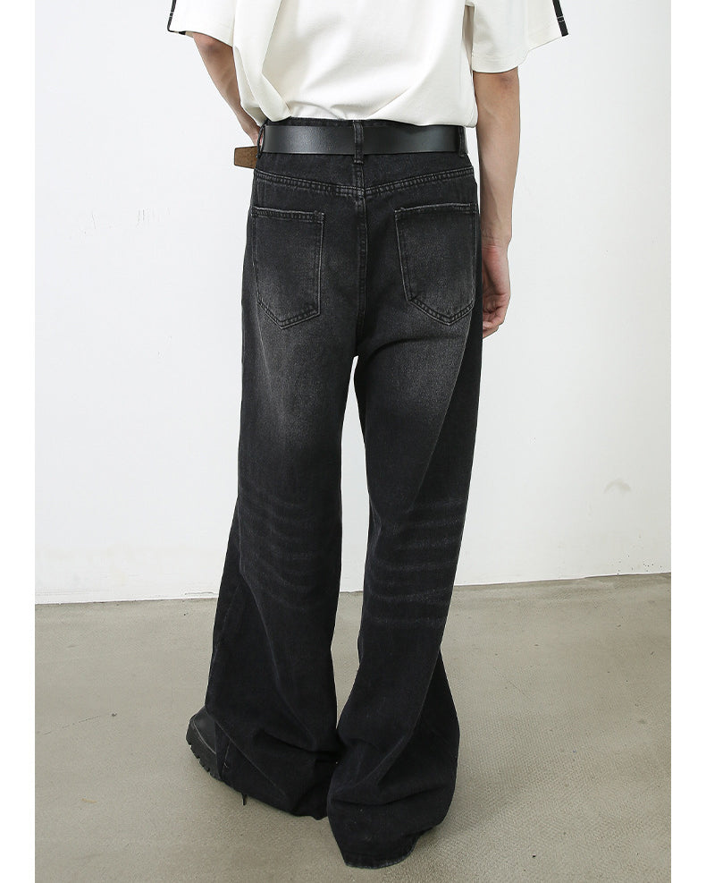 A back view of model in oversized white top and wide-leg black denim jeans. Shows detail of traditional back pockets and leather belt.