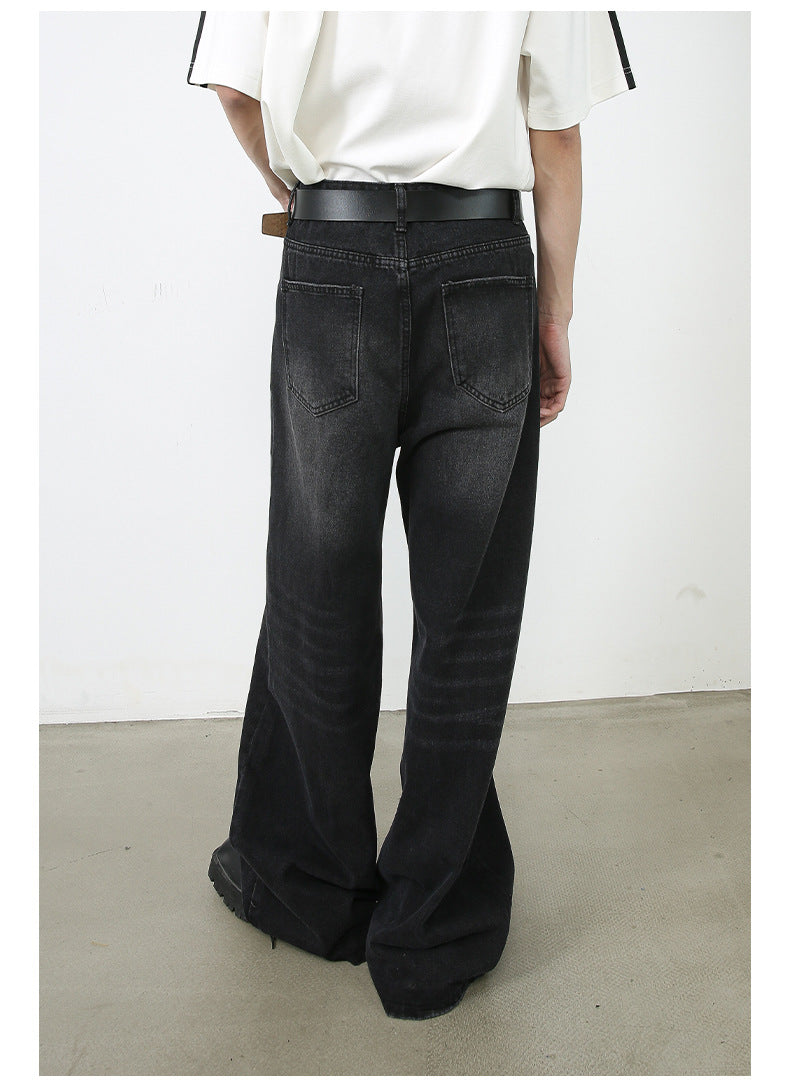 A back view of model in oversized white top and wide-leg black denim jeans. Shows detail of traditional back pockets and leather belt.