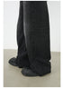 A close-up of black wide-leg denim jeans pooling at ankles over chunky platform shoes. Shows detailed hem construction and extra-long silhouette against neutral floor