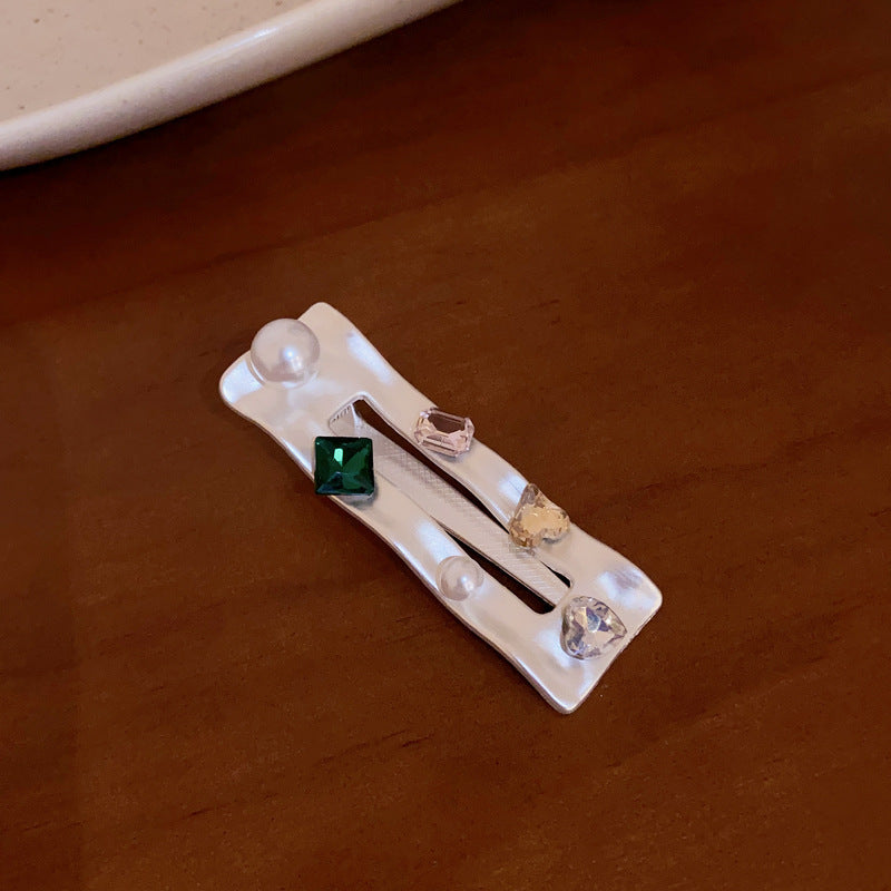 Close-up of rectangular white hair clip decorated with pearls and emerald-colored crystal