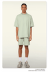 A man with braided hair wearing a mint green oversized t-shirt and shorts set, styled with silver chain necklace, white socks, and chunky sneakers