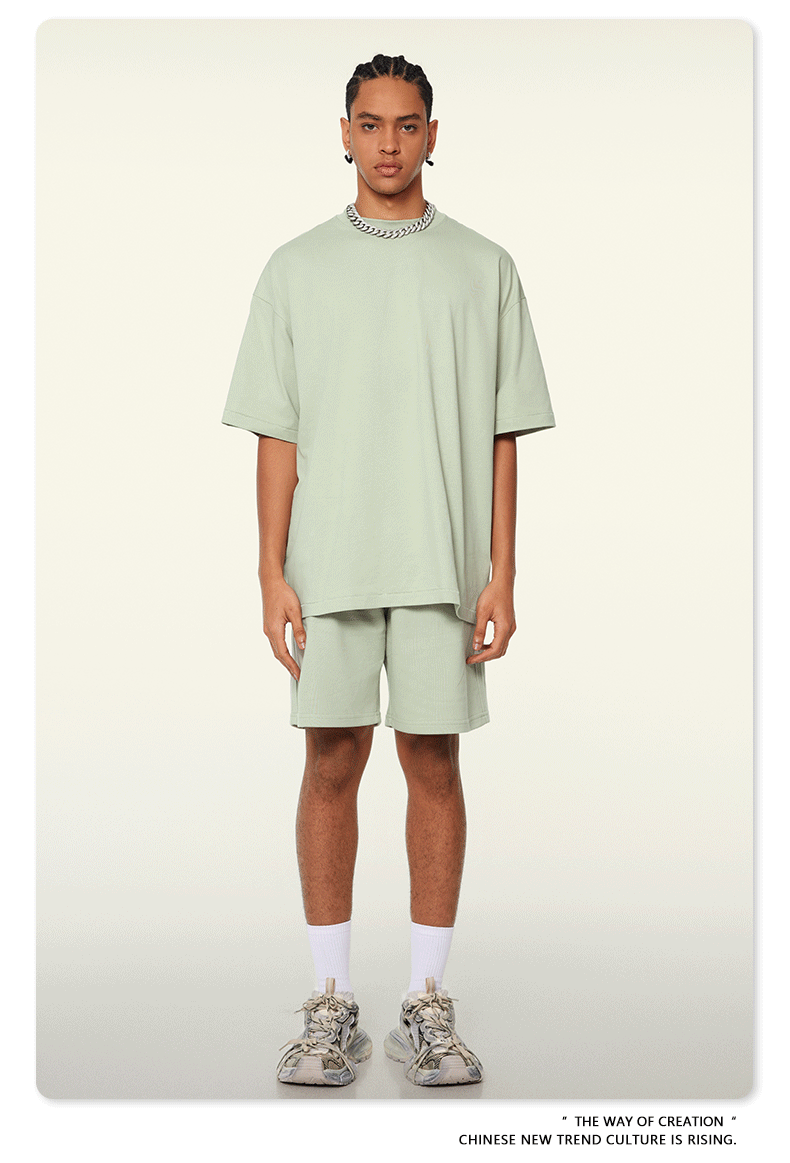 A man with braided hair wearing a mint green oversized t-shirt and shorts set, styled with silver chain necklace, white socks, and chunky sneakers