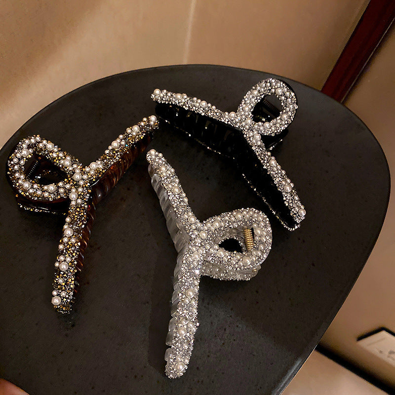 Three crystal and pearl-embellished hair clips displayed on black surface, featuring bow designs in clear and tortoiseshell finishes