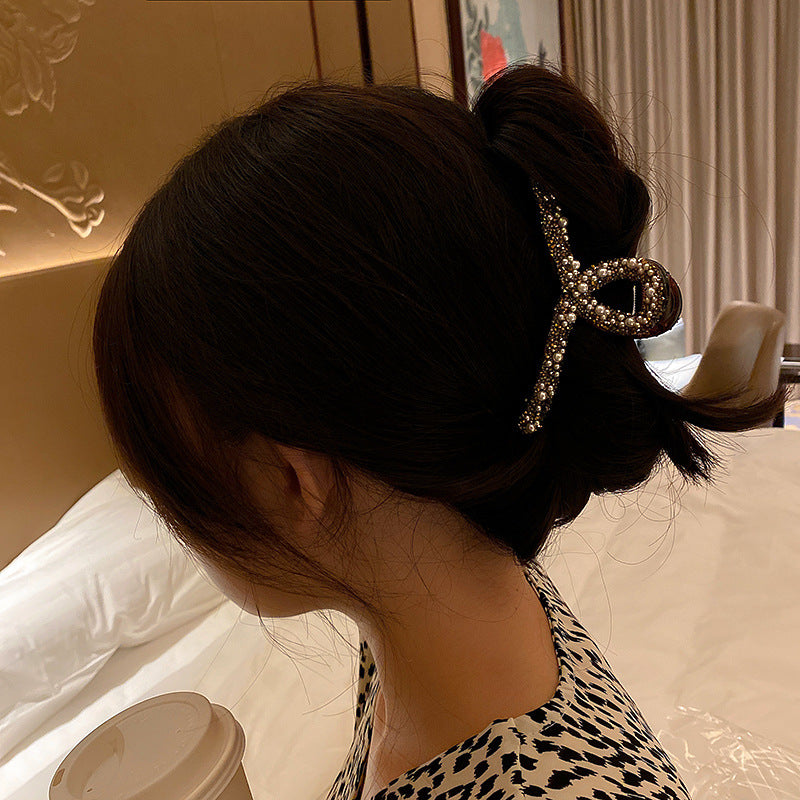 Woman wearing crystal-adorned bow hair clip in dark updo, wearing leopard print top, side view in warm indoor lighting