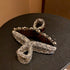 Close-up of crystal and pearl-encrusted hair clips in bow design on dark surface, one clear and one tortoiseshell finish