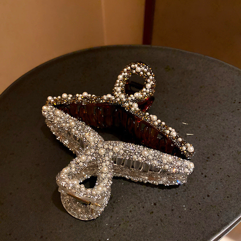 Close-up of crystal and pearl-encrusted hair clips in bow design on dark surface, one clear and one tortoiseshell finish