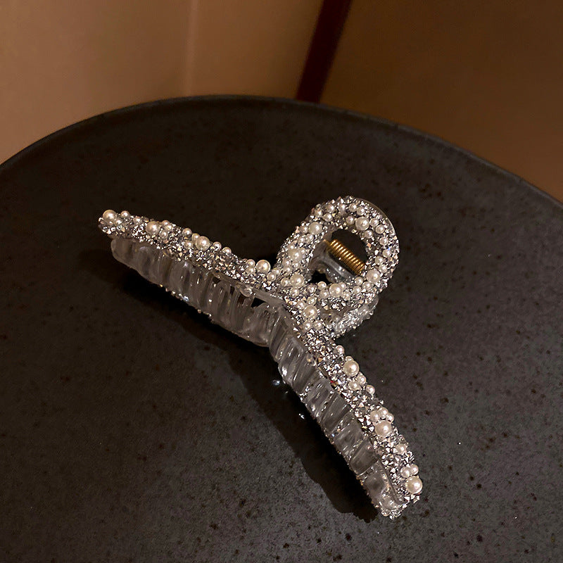 Crystal-embellished bow hair clip with pearl accents displayed on dark surface, showing clear grip texture