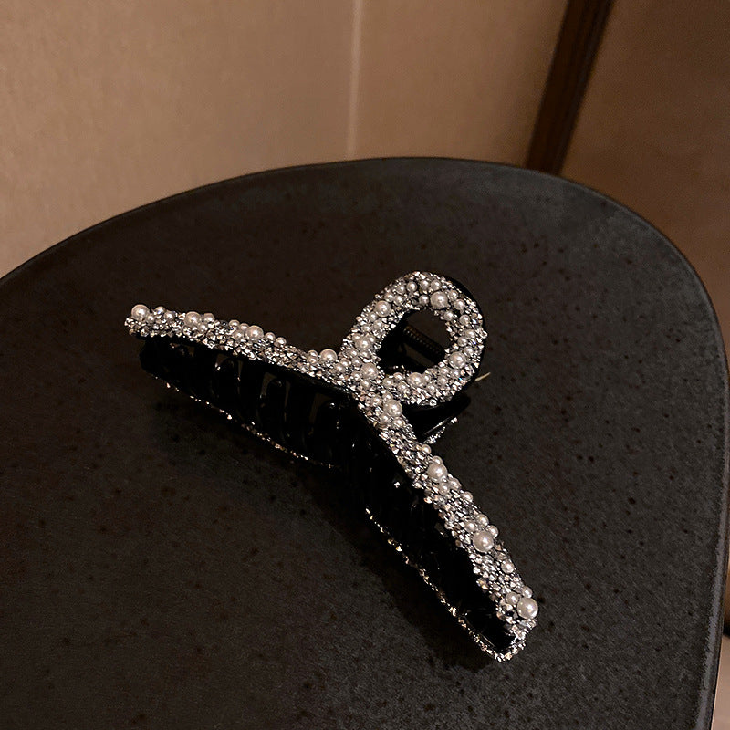 Pearl and crystal bow hair clip with black grip showing detailed embellishment on dark background