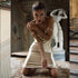 Model kneeling in champagne silk midi dress with classical statue in background, showing editorial styling