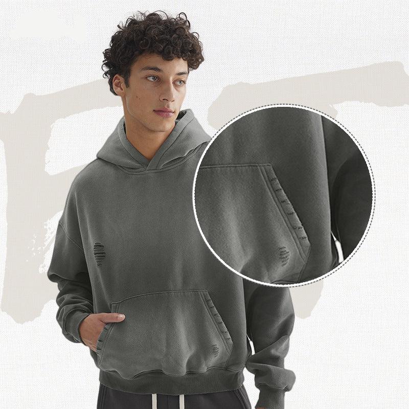Model wearing grey hoodie with distressed details and hand in pocket, with magnified circular detail of pocket area