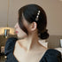 A woman in a black puff-sleeve dress wearing her hair in a low bun, styled with an elegant pearl and black velvet hair clip