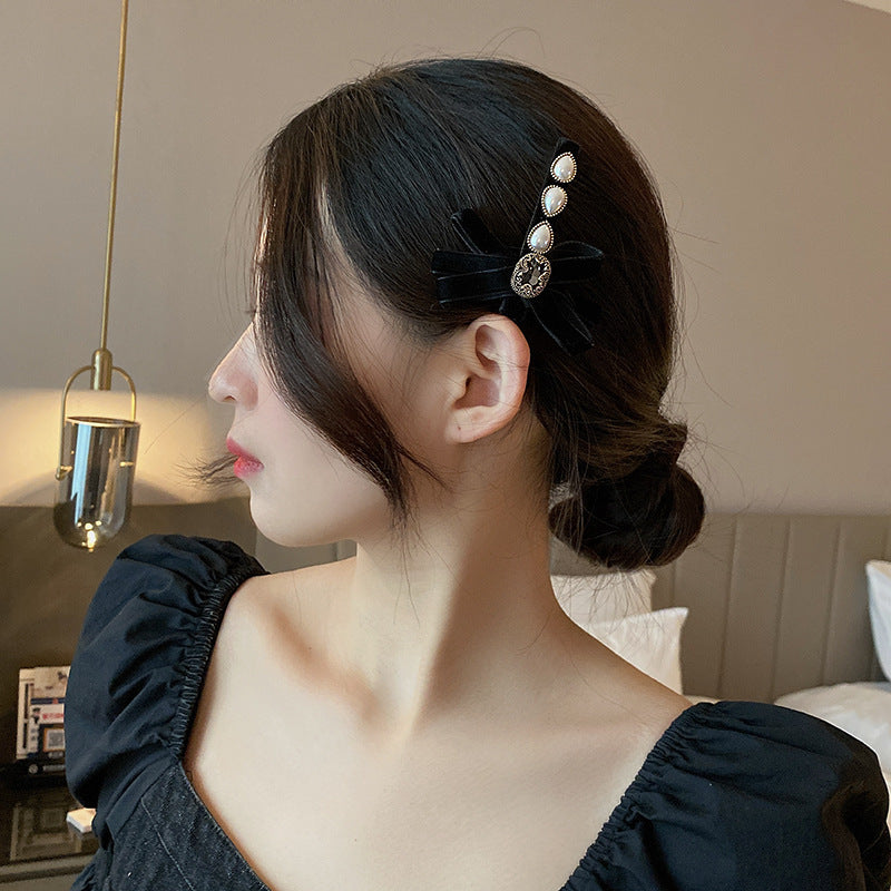 A woman in a black puff-sleeve dress wearing her hair in a low bun, styled with an elegant pearl and black velvet hair clip