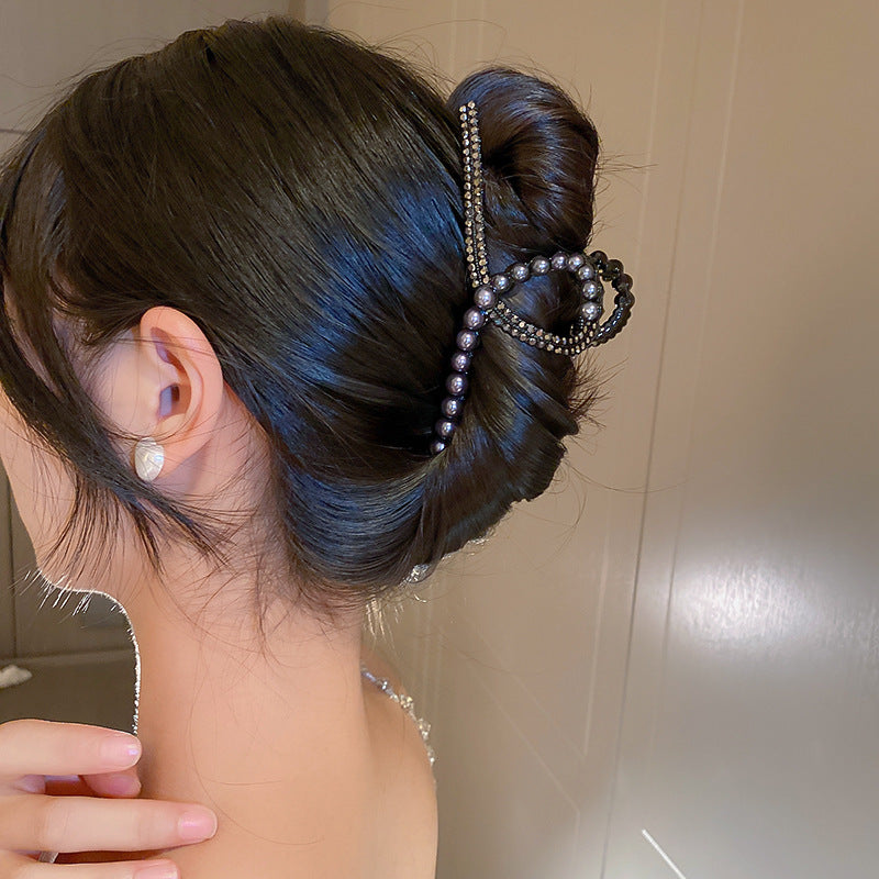 A woman wearing a sleeveless top with her dark hair styled in a bun, fastened with a pearl and crystal bow clip