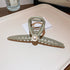 A matte beige hair claw clip with a pearl accent, photographed on a white surface near a Burberry logo