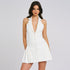 A woman wearing a white halterneck blazer mini dress with deep V-neckline and pleated side detail, posing against gray background