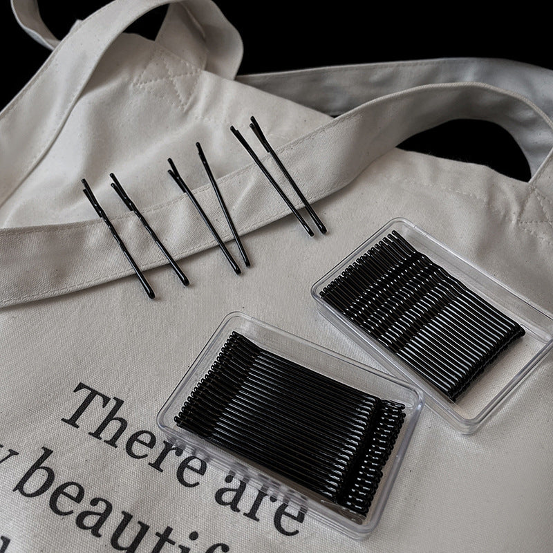 Black bobby pins and storage boxes on white canvas bag with text, minimalist beauty accessory organization