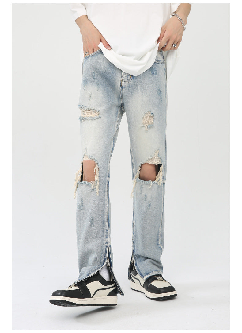 Model wearing light wash distressed jeans with knee rips, ankle zips, white tee and black/white sneakers on white backdrop