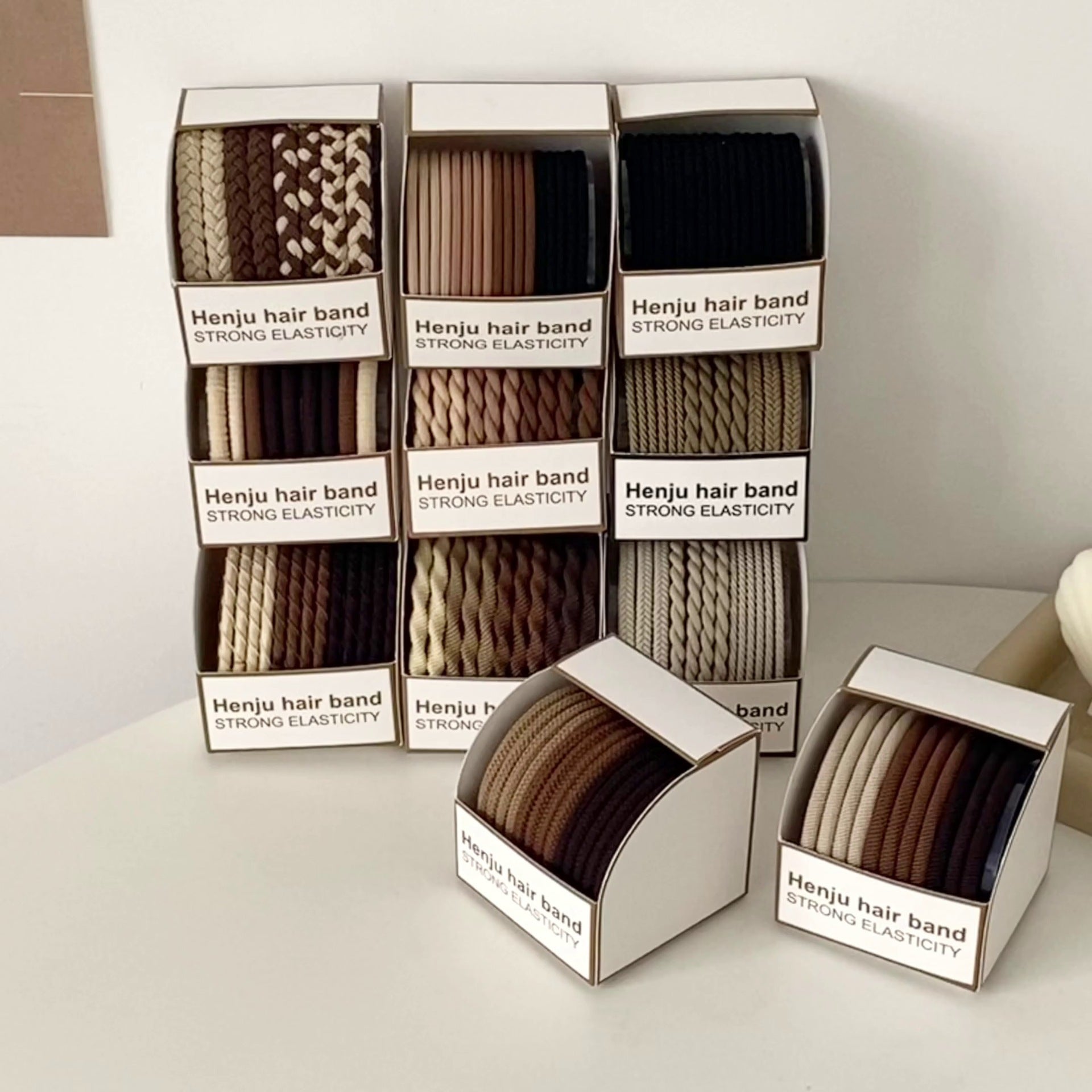 Stacked display of Henju hair band boxes showing different textures and colors including black, brown and beige, labeled "Strong Elasticity"