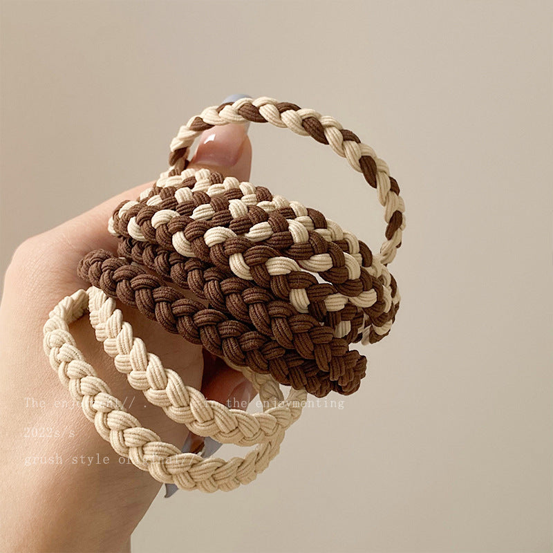 Hand holding braided elastic hair bands in cream and brown colors, showing different braiding patterns and textures